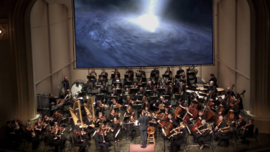 Boulder Phil plays music about stars and astronomers and planets in front of screen displaying beautiful space images